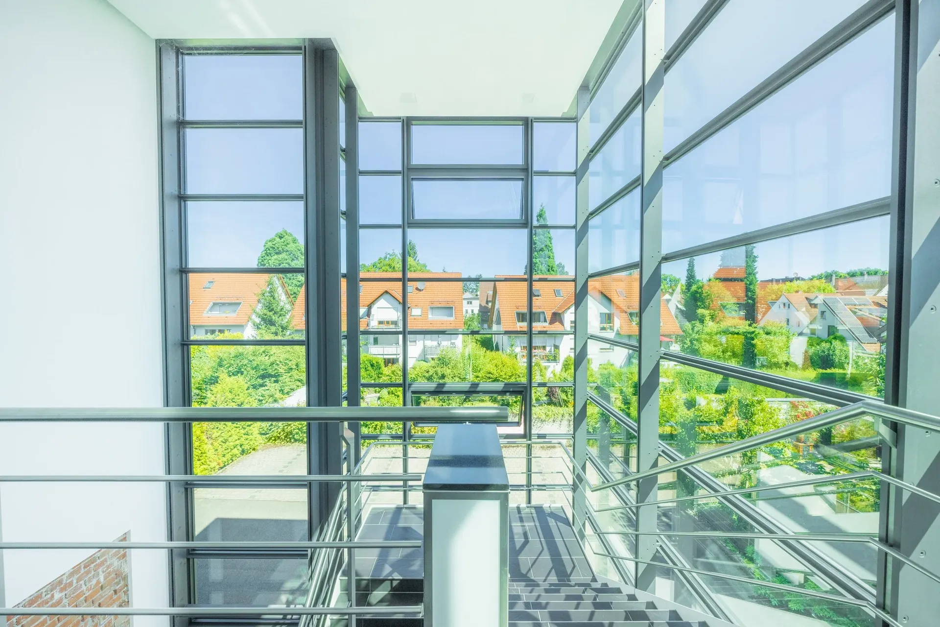 Verglastes Treppenhaus mit Blick auf Satteldächer und Grünflächen — Immobilienfotografie Maurice Veith