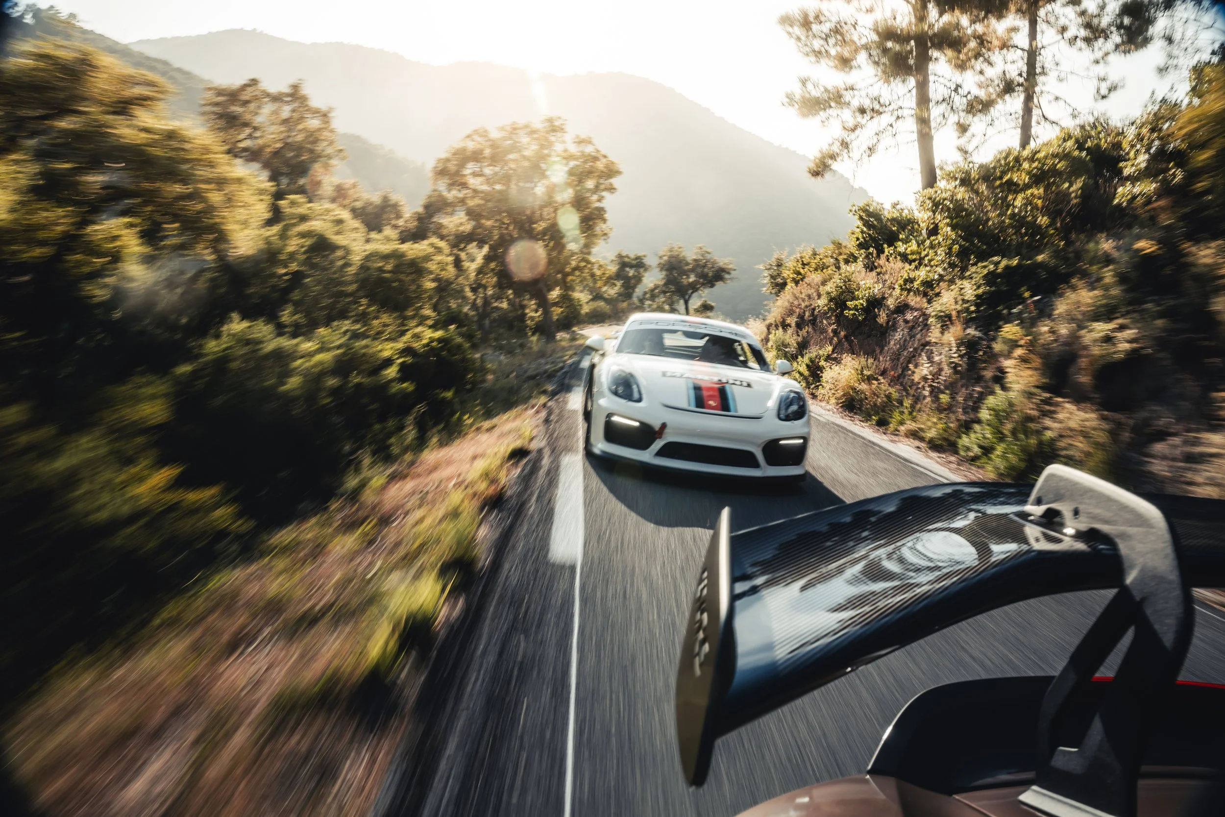 Weißer Porsche Cayman GT4 in Fahrt auf einer Bergstraße — Automobilfotografie Maurice Veith